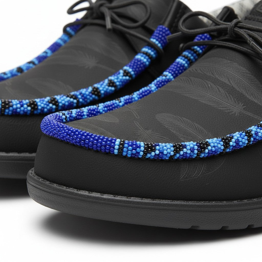 All Nations Designs &amp; More black Hey Dude slip-on shoes featuring blue and black hand-beaded feather pattern detail.
