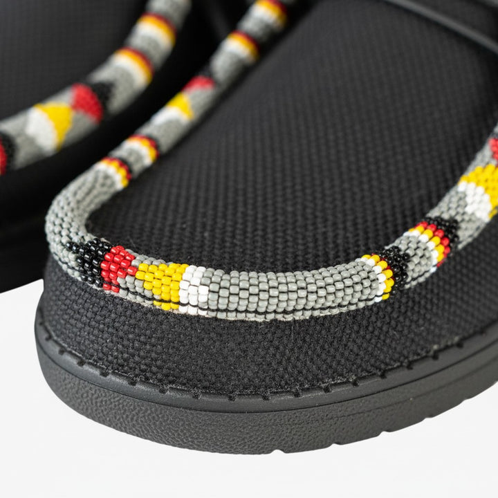 All Nations Designs &amp; More black mesh slip-on shoes featuring traditional hand-beaded trim in red, yellow, and grey.