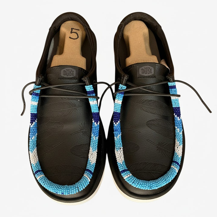 All Nations Designs &amp; More Hey Dude slip-on shoes in black with laser-etched feathers and vibrant blue hand-beaded trim.
