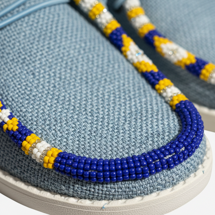 All Nations Designs &amp; More hand-beaded blue mesh slip-on shoes with yellow, white, and blue geometric beadwork.