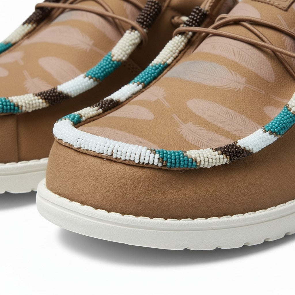 All Nations Designs &amp; More brown Hey Dude slip-on shoes featuring custom hand-beaded feather patterns and white soles.