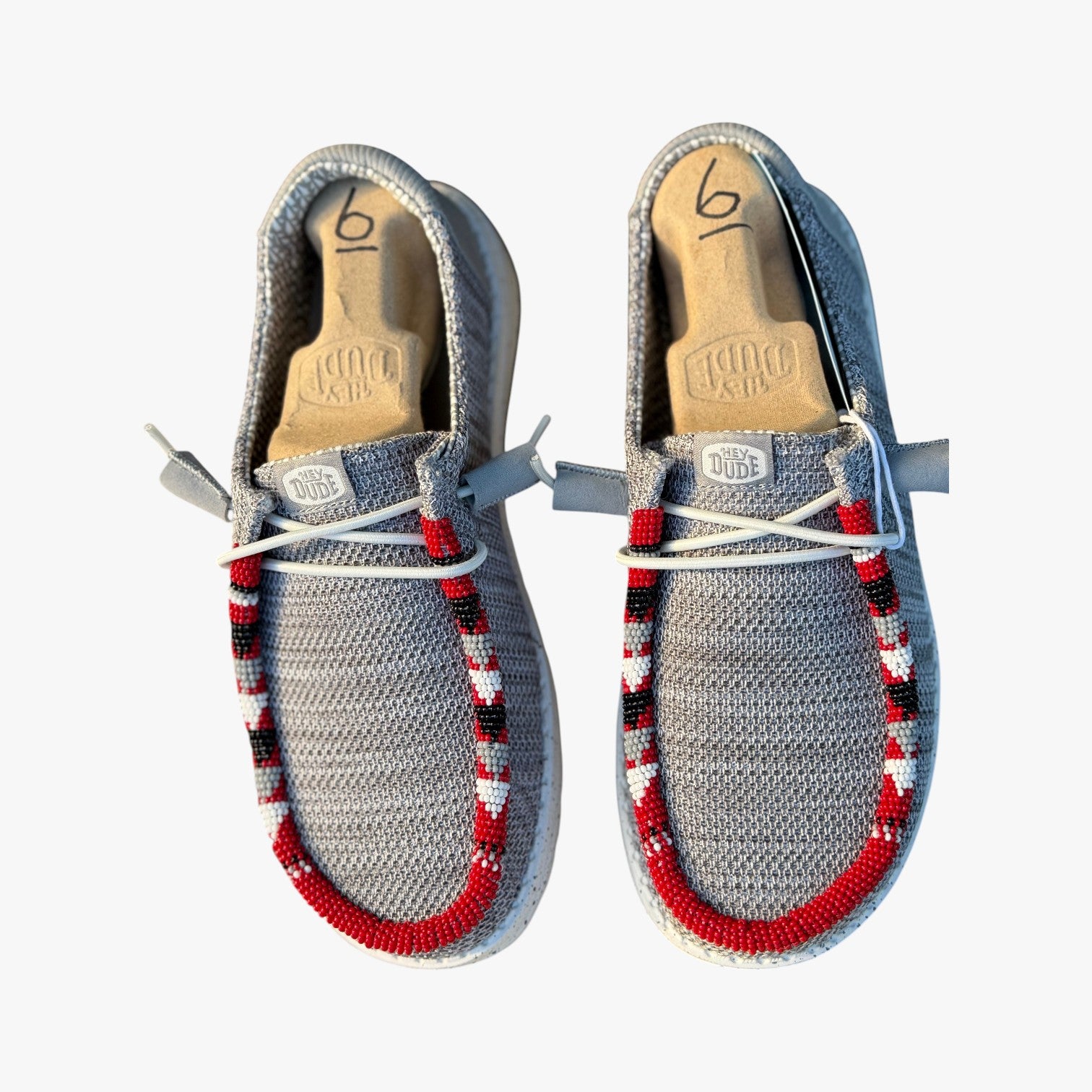 All Nations Designs & More gray mesh Hey Dude slip-on shoes featuring custom red, black, and white hand-beaded trim.