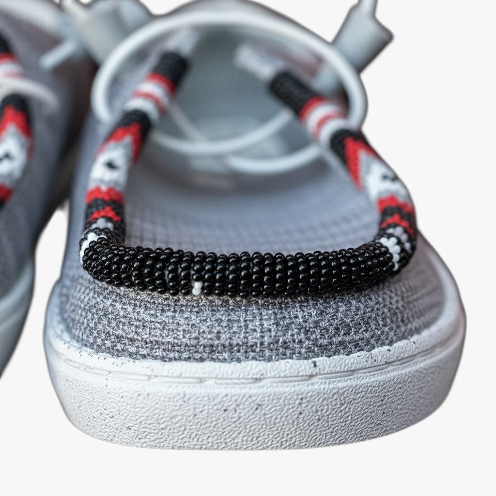 All Nations Designs &amp; More light gray Hey Dude slip-on shoes featuring intricate hand-beaded trim in black, red, and white.