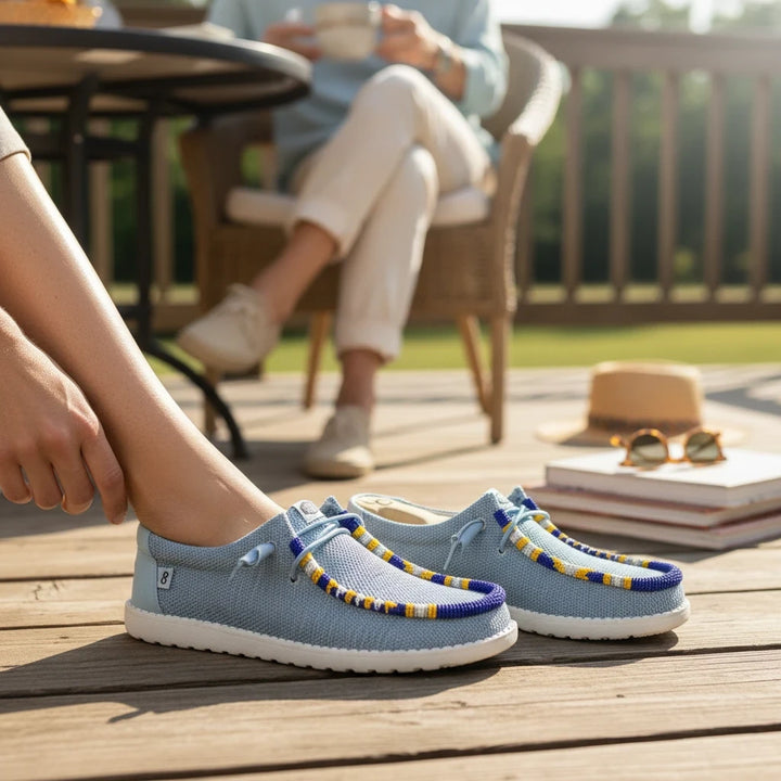 All Nations Designs &amp; More hand-beaded blue mesh slip-on shoes worn on a wooden deck with casual outdoor setting