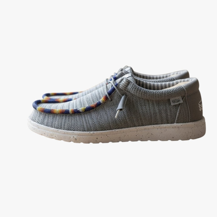 All Nations Designs &amp; More gray mesh Hey Dude slip-on shoes featuring custom colorful hand-beaded trim on a wooden table