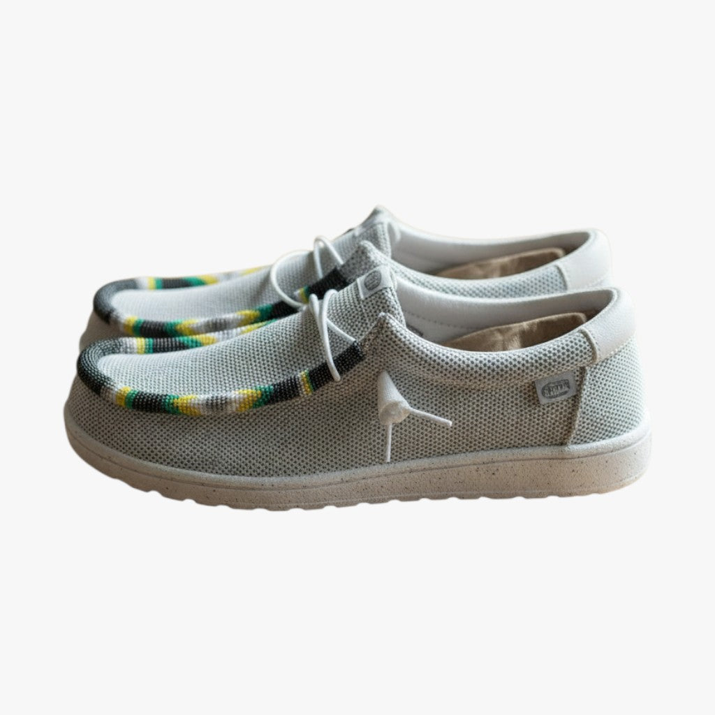 All Nations Designs &amp; More gray mesh slip-on shoes featuring custom hand-beaded trim on a wooden table.