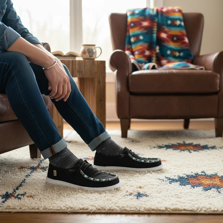 All Nations Designs &amp; More black mesh slip-on shoes featuring custom hand-beaded trim worn with jeans in a cozy room.