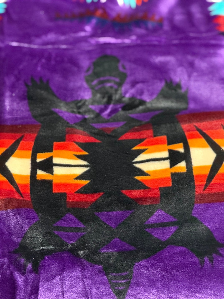 Purple Turtle double-ply blanket close-up showing the turtle motif, geometric borders, and soft fabric texture.
