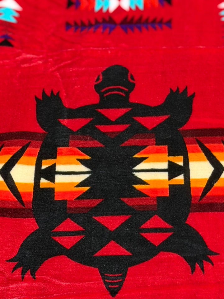 Red Turtle double-ply blanket close-up showing the turtle motif, geometric borders, and soft fabric texture.
