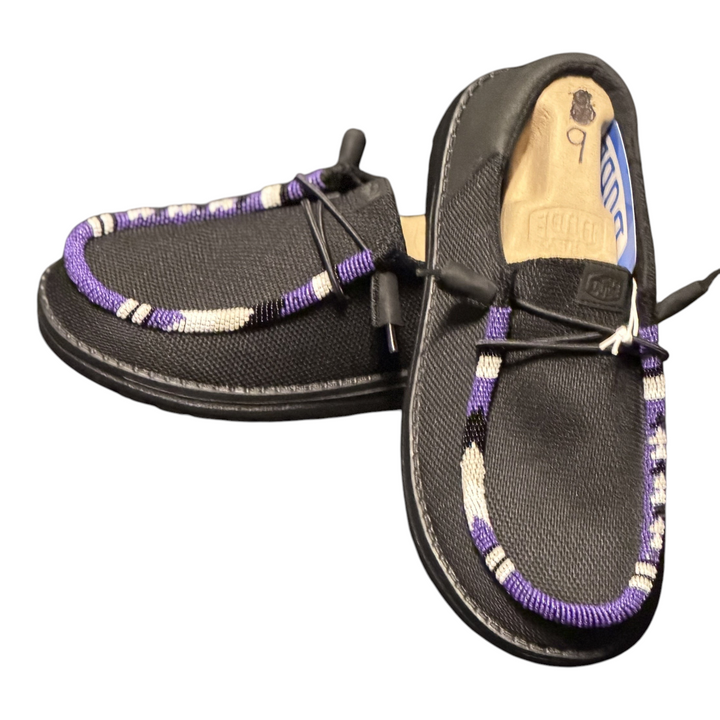 Women’s size 9 black Hey Dude Wendy shoes with purple, white and black hand-beaded trim — angled pair detail
